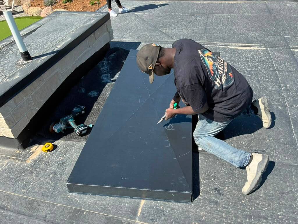 Laying out cut lines on a custom steel chase cover panel beside a stone chimney chase