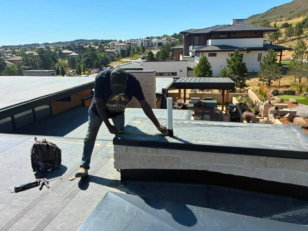 Measuring a chimney chase cover around the flue pipe with a tape measure on a Colorado roof