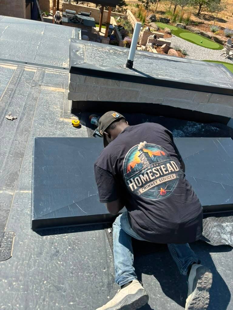 Fitting a black metal chase cover panel to a stone chimney chase on a modern Colorado home